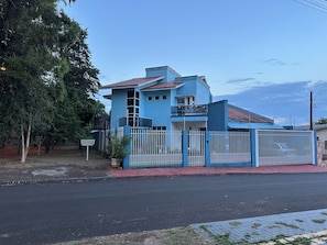 A two-story house with a red-tiled roof, a white fence, and a paved driveway. - Recanto Luna foz (Foz do Iguaçu)