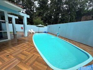 A swimming pool with a wooden deck, white lounge chairs, and a covered area with an umbrella.