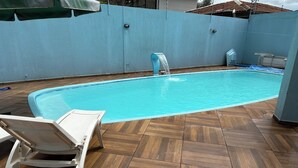 Una piscina con fuente, una silla de descanso blanca y una terraza con baldosas.
