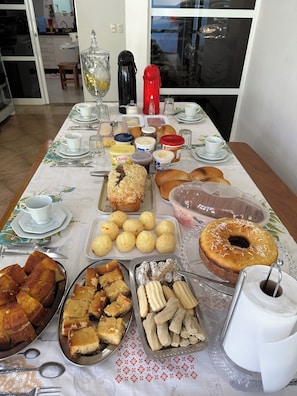 A dining table with various food items, utensils, and a coffee machine. - Recanto Luna foz (Foz do Iguaçu)