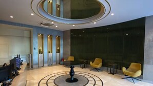Eine Lobby mit einem runden Tisch in der Mitte, einer Sitzecke mit gelben Stühlen und einem Empfangstresen.