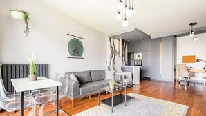 Ein modernes Wohnzimmer mit grauem Sofa, einem Esstisch mit Stühlen, einem Couchtisch und einer Küchenzeile im Hintergrund.