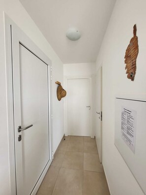 A hallway with white walls, a white door, and a ceiling light fixture.