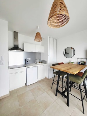 Une cuisine moderne avec des meubles blancs, un lave-vaisselle, une machine à café et une table à manger en bois, assortie de chaises noires.