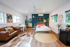 A modern bedroom with a bed, a sofa, a dining area, and a kitchen in the background.