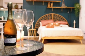 A bed with a wooden headboard, a bedside table with candles, and a bottle of wine on a round table.
