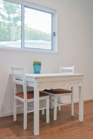 Een witte eettafel met twee stoelen, een blauwe potplant en een raam met uitzicht op bomen.