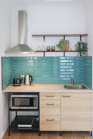 Eine kleine Küche mit blaumetallfarbener Spritzschutzleiste, Edelstahlgeräten und einer Holzarbeitsplatte.