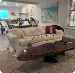 A living room with a sofa, coffee table, and a dining area in the background.