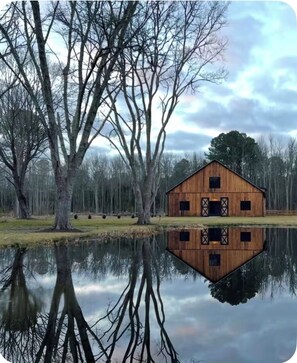 A wooden barn with a reflection in a calm body of water, surrounded by leafless trees and a cloudy sky. - Get away from it all while you stay under the stars (Ocean City)