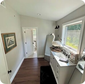 A narrow hallway with a wooden floor, a white door leading to a bathroom, and a vanity with a mirror and sink. - Get away from it all while you stay under the stars (Ocean City)