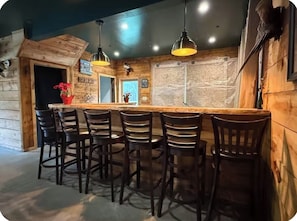 A rustic interior with a wooden bar and bar stools, a stone wall, and a hanging light fixture.