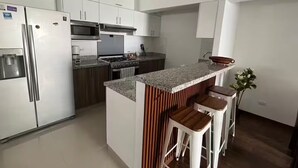 Una cocina moderna con gabinetes blancos, electrodomésticos de acero inoxidable, encimera de granito y taburetes de madera.