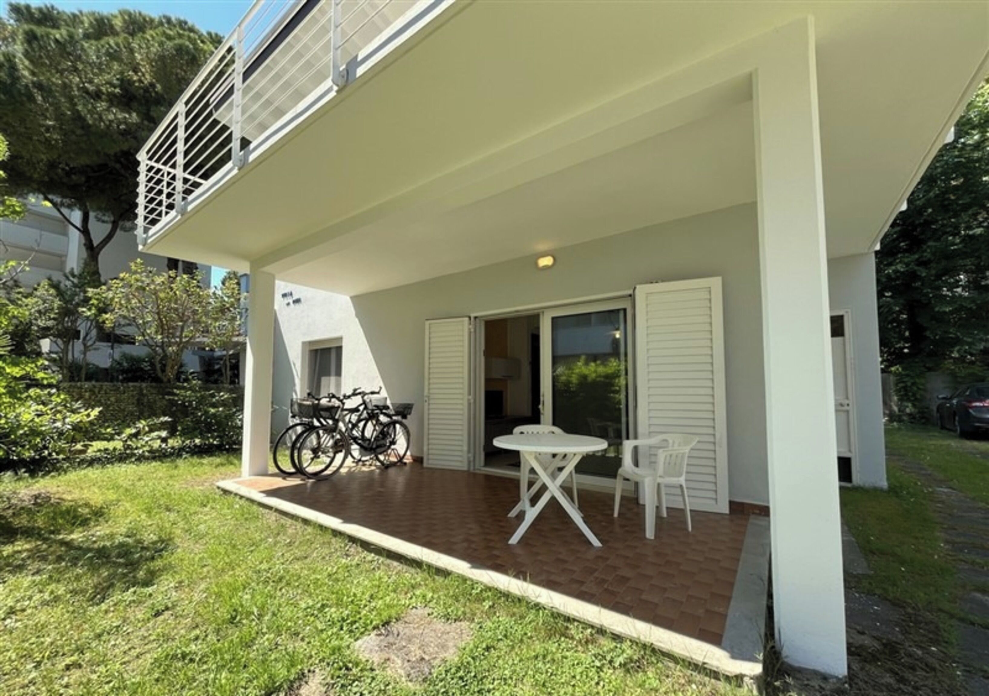 Um edifício de dois andares com um alpendre coberto, que inclui uma mesa, cadeiras, bicicletas e uma porta que dá para o interior.