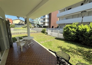 A covered outdoor area with a patio table and chairs, a bicycle, and a white fence. - Quiet Apartment Near the sea (Lignano Sabbiadoro)