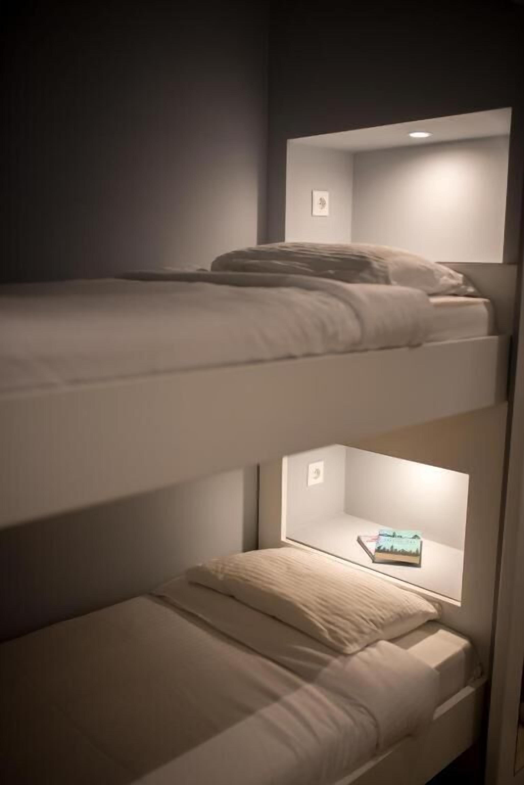 Una cama litera con un estante pequeño debajo de la cama superior y una lámpara encima.