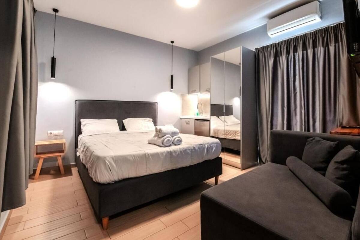 A modern hotel room with a large bed, a sofa, a bedside table, and a mirror.