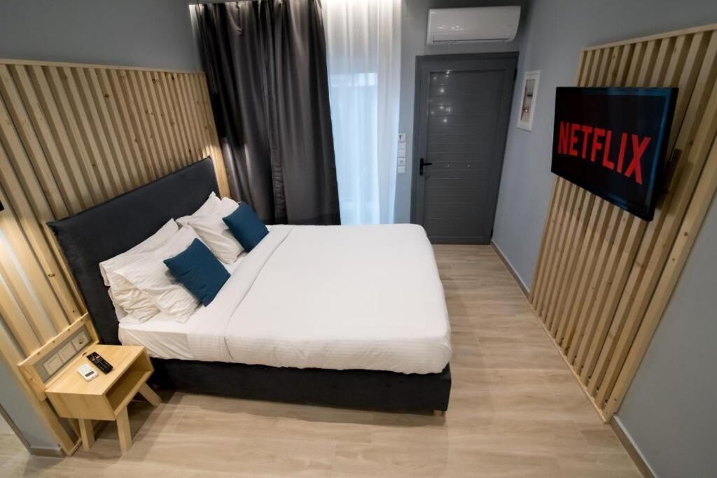Una habitación de hotel con cama, televisor montado en la pared, una mesita de noche y una puerta.