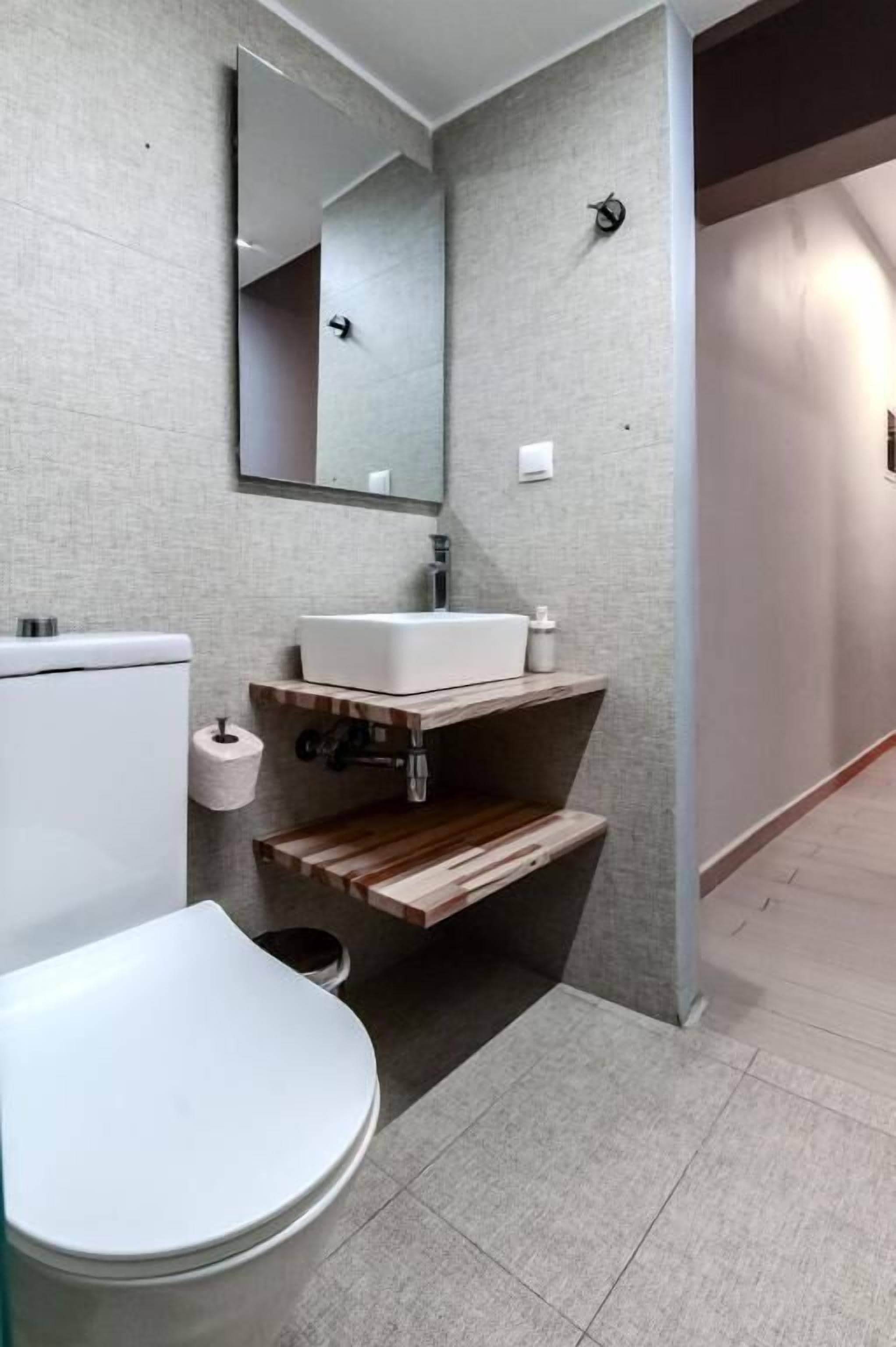 A bathroom with a white toilet, a sink with a wooden vanity, a mirror, and a towel rack.