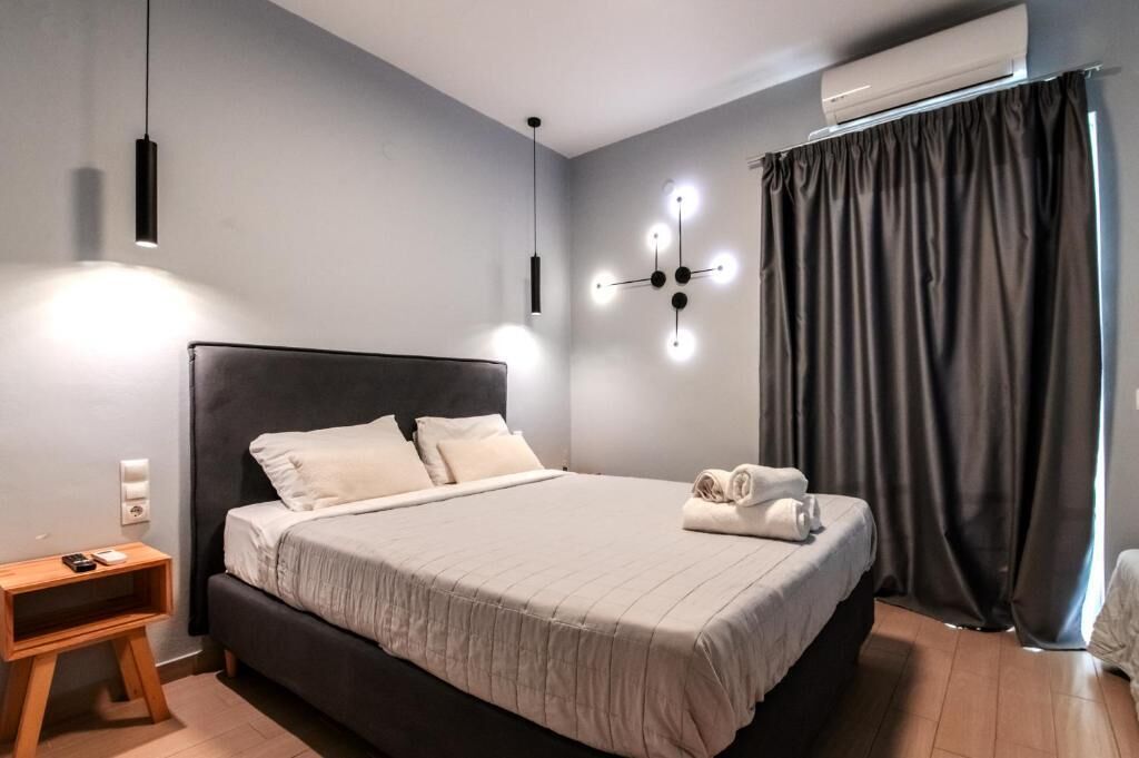 Un dormitorio moderno con una cama grande, mesitas de noche, una lámpara de pared y un ventanal con cortinas.