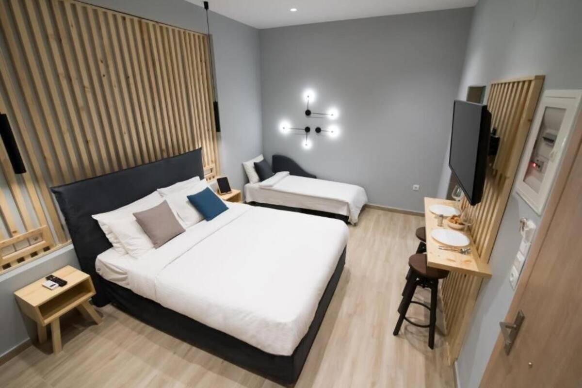 A hotel room with a large bed, bedside tables, a desk with a chair, a TV, and a wall-mounted light fixture.