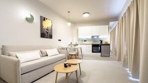 Una sala de estar moderna con un sofá, dos mesas redondas y una cocina al fondo.