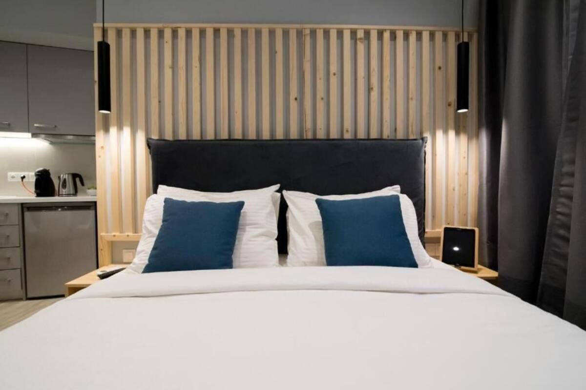 A hotel room with a bed, bedside tables, a wooden slat wall, and a modern light fixture.