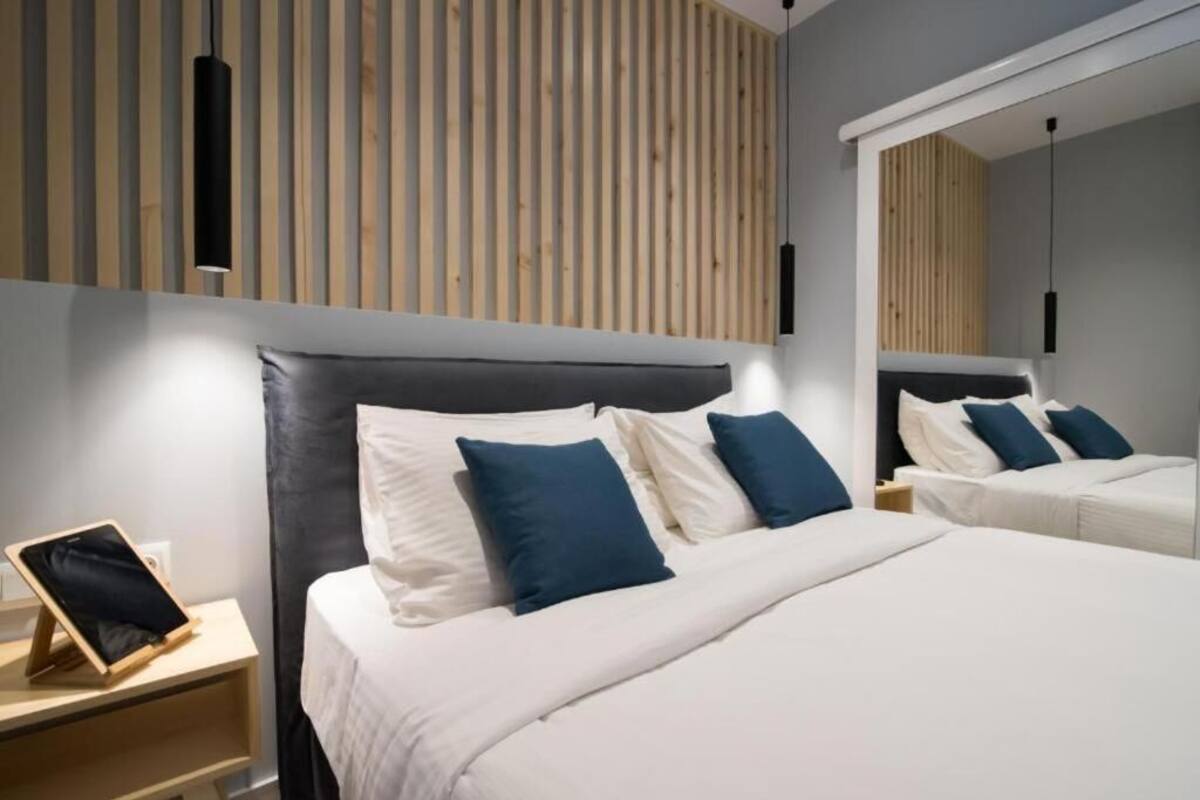 A modern hotel room with a large bed, bedside tables, a mirror, and a wooden slat wall.