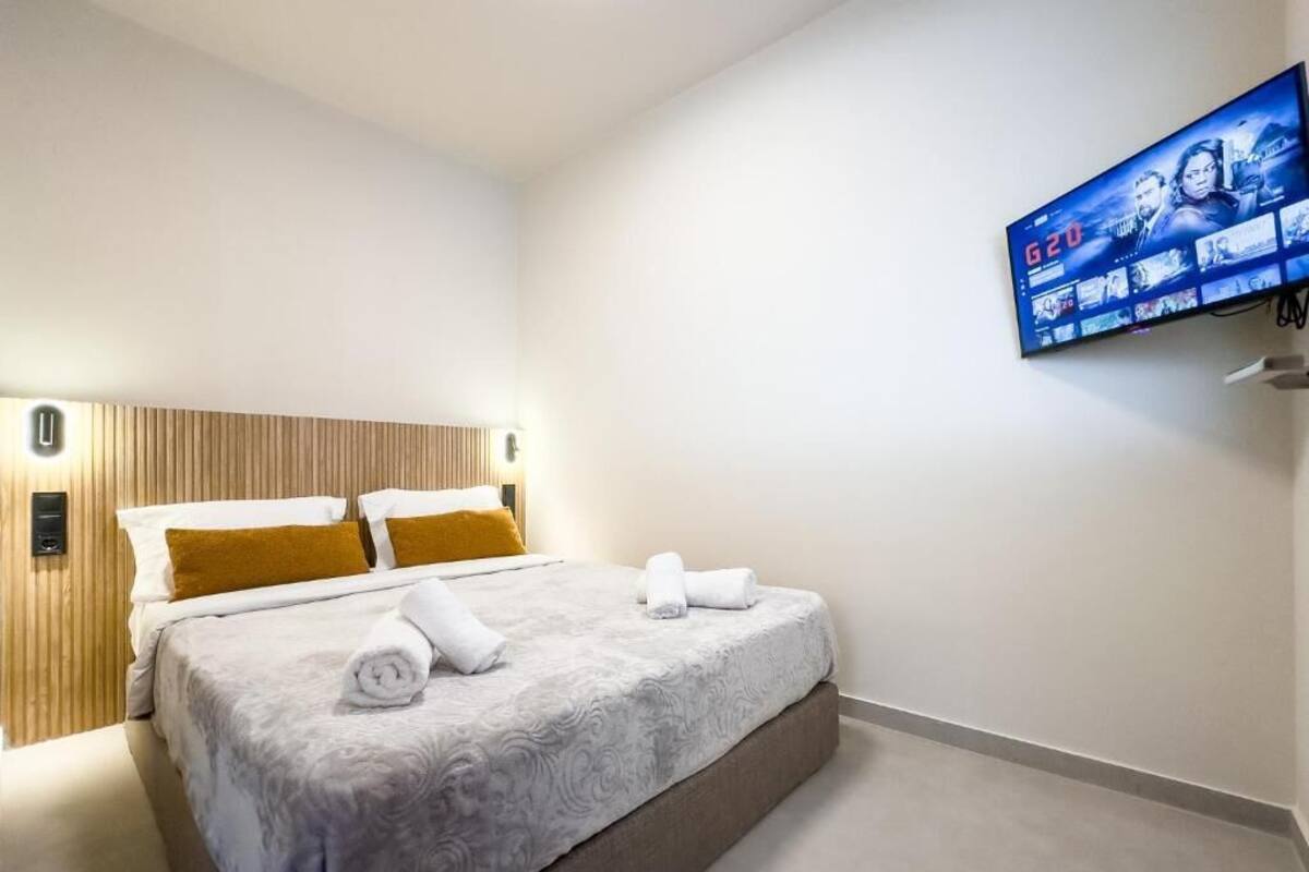 A hotel room with a bed, a television mounted on the wall, and a wooden headboard.