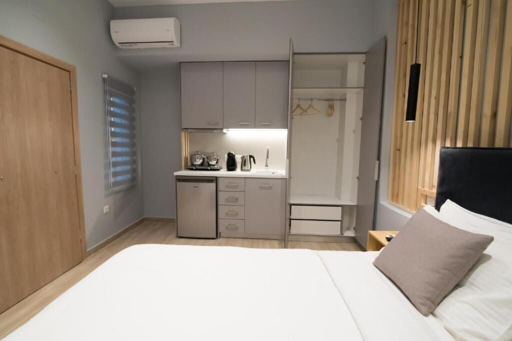 A compact room with a bed, a small kitchenette, a wardrobe, and a window with blinds.