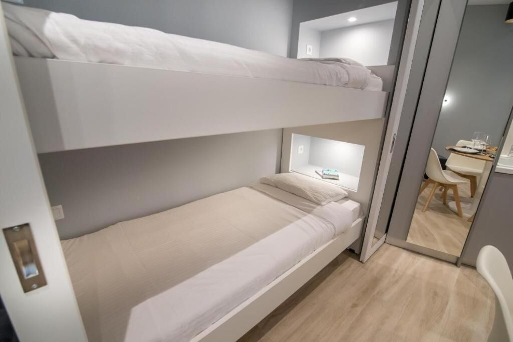 A bunk bed room with a desk and chair, a mirror, and a small table with a glass.