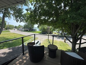 Un espace extérieur abrité, aménagé avec des meubles en osier, offrant une vue sur la rue et un arbre.