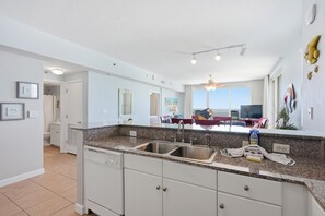 A modern kitchen with granite countertops, a double sink, and a dining area with a view. - Shores of Panama #1301, 3BR/3BA, Wrap-around Balcony! (Panama City Beach)