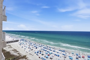 Ein Strand mit vielen Sonnenschirmen und Menschen, ein klarer Himmel und Blick auf den Ozean.