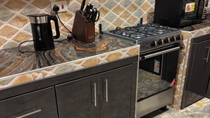 A kitchen with a gas stove, a coffee maker, and a knife block. - Beautiful 2-bedroom terrace with AC and fan in all rooms in a gated community. (Amrahia)