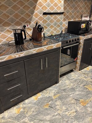 A kitchen with a gas stove, a coffee maker, and a knife block. - Beautiful 2-bedroom terrace with AC and fan in all rooms in a gated community. (Amrahia)