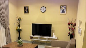 A living room with a flat-screen TV, two sofas, a coffee table, a clock, and wall art. - Beautiful 2-bedroom terrace with AC and fan in all rooms in a gated community. (Amrahia)