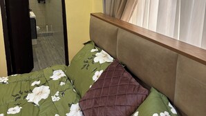 A bedroom with a bed, a mirror, a window with curtains, and a bathroom visible through an open door. - Beautiful 2-bedroom terrace with AC and fan in all rooms in a gated community. (Amrahia)
