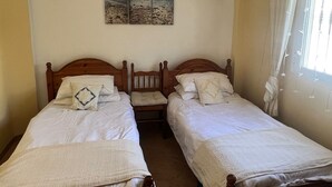 A bedroom with two wooden beds, white bedding, a wall-mounted artwork of a beach, and a window with curtains.