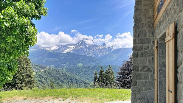 Un edificio de piedra con vistas a montañas nevadas y un valle boscoso.