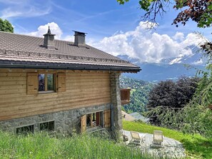 Eine Holzhütte mit Steinunterbau und Ziegeldach, mit Blick auf eine gebirgige Landschaft.