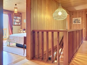 Ein Holzinnenraum mit einem Bett, Bücherregalen, einer Treppe und einer Hängeleuchte.