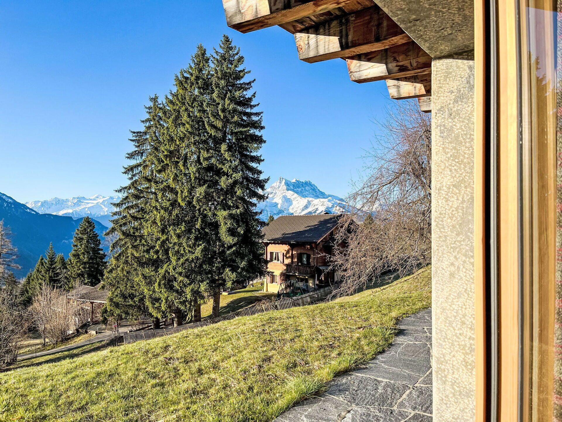 A mountain cabin with a stone exterior, surrounded by trees and a clear view of snow-capped mountains.