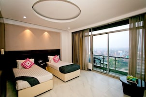 Quarto de hotel com duas camas, uma janela grande com vista para a cidade, varanda e design moderno no teto.
