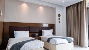 Ein Hotelzimmer mit zwei Betten, einem hölzernen Kopfteil, einem Nachttisch mit Telefon und einem großen Fenster mit Vorhängen.