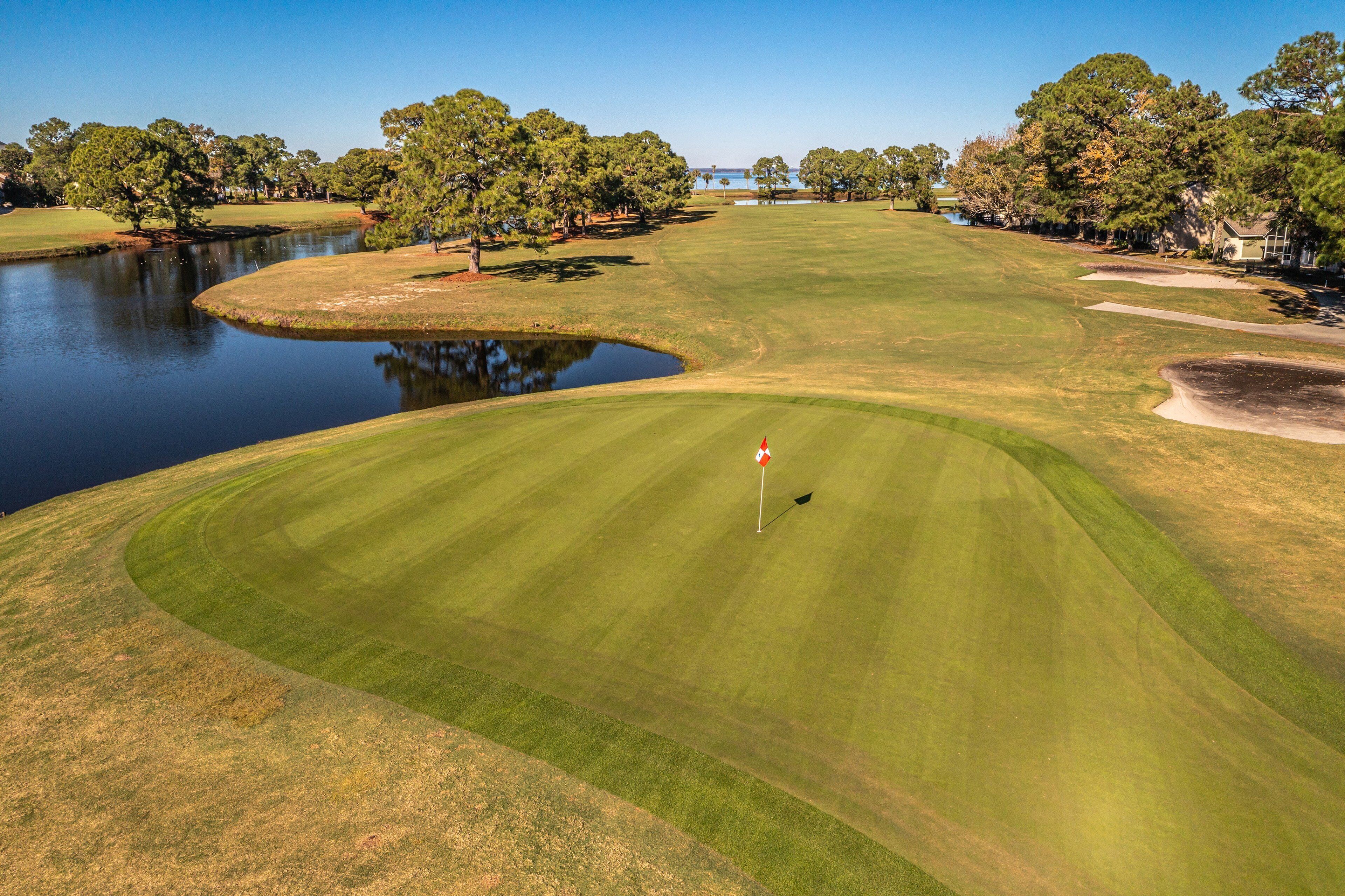Un campo de golf con un estanque, árboles y un marcador de bandera.
