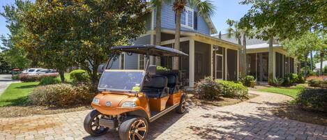 A golf cart parked in front of a building with a covered porch and palm trees.