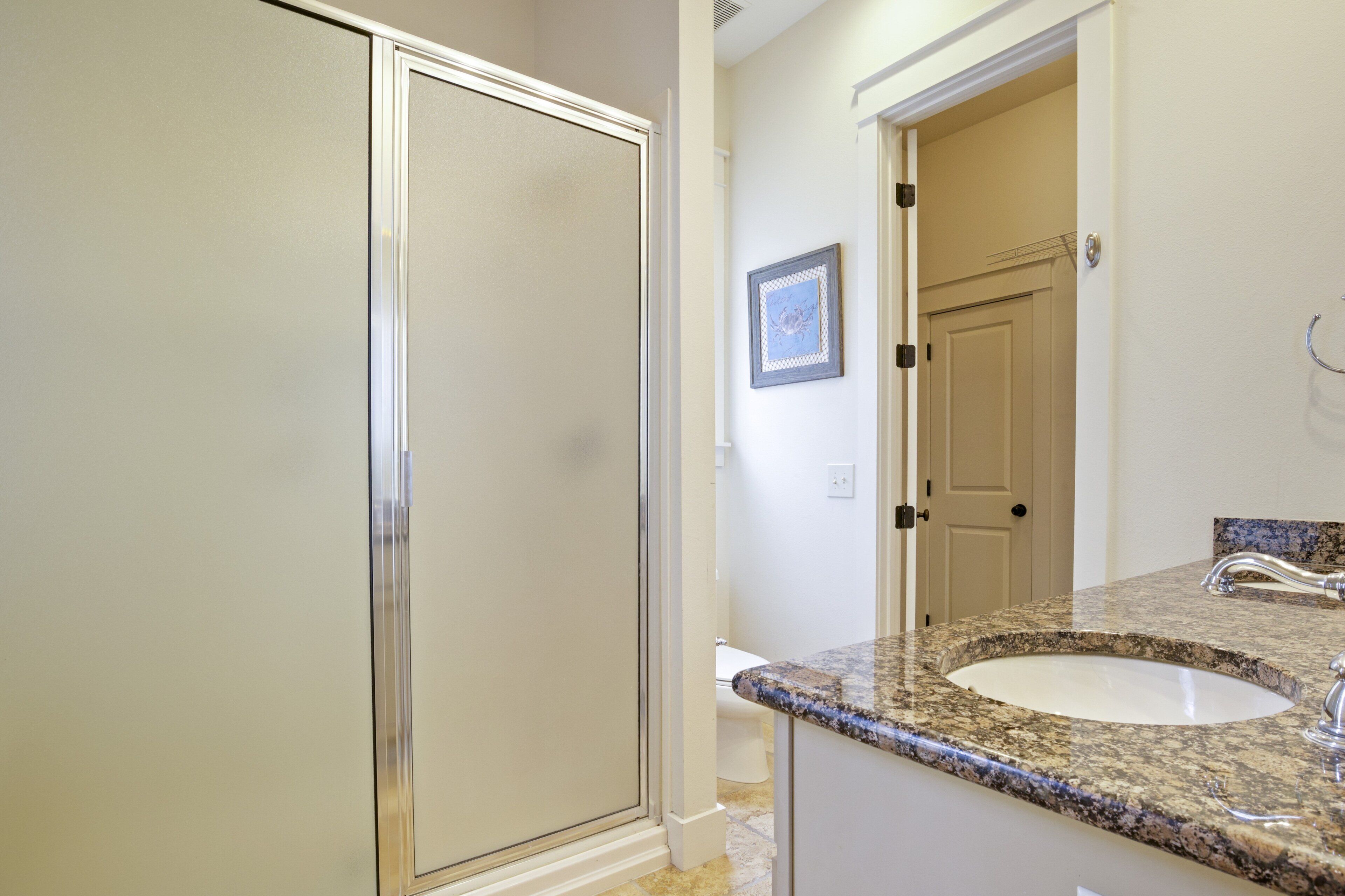 A bathroom with a shower, toilet, sink, and a framed picture on the wall.