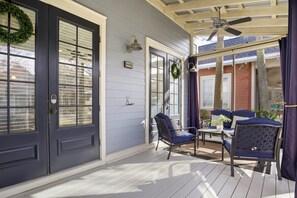 Ein überdachter Balkon mit Deckenventilator, zwei Glastüren und einer Sitzgruppe mit blauen Stühlen und einem Tisch.