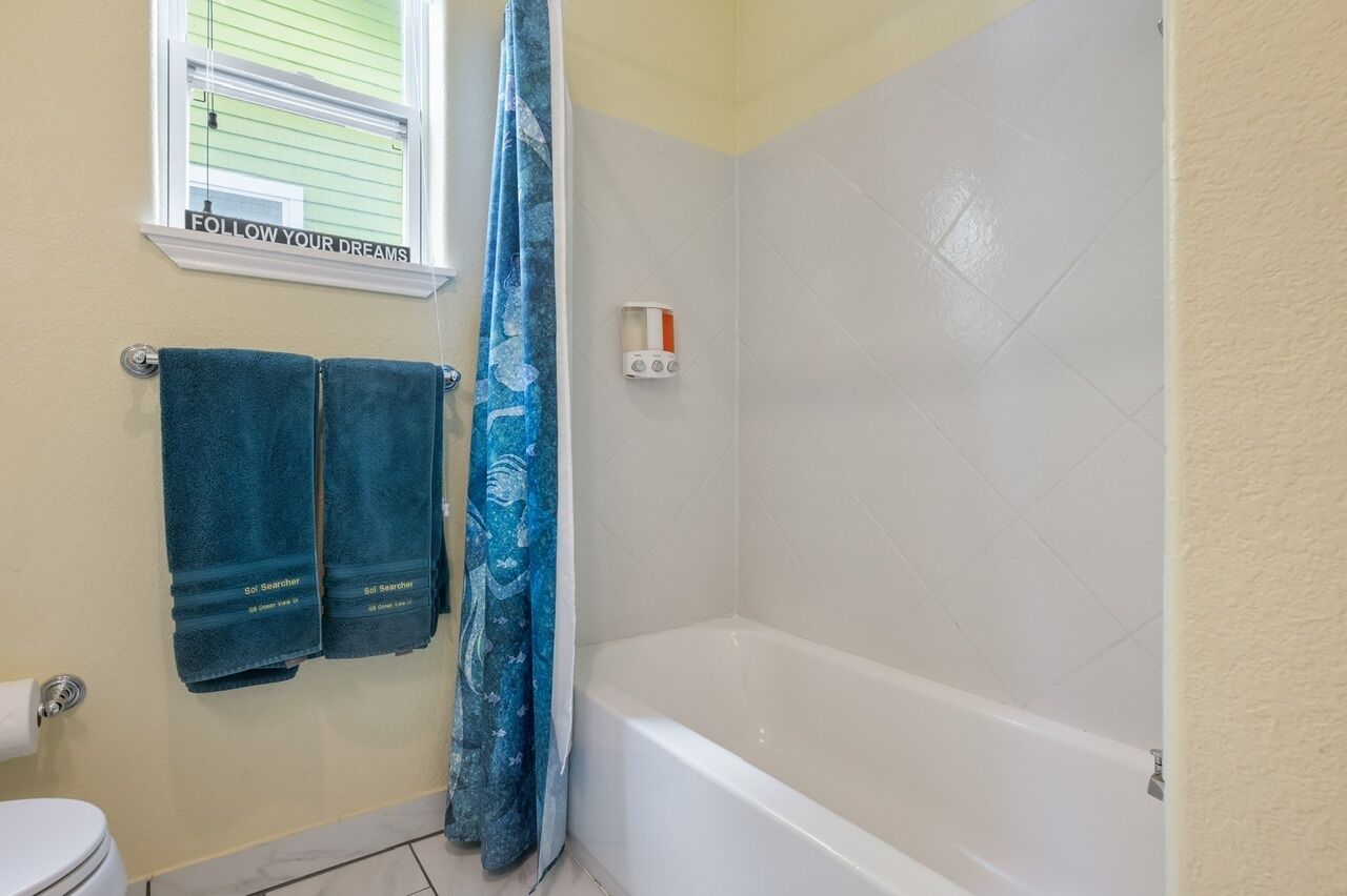 A bathroom with a bathtub, two towels, a shower curtain, and a window with a motivational quote.